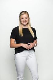 Allison is posing hands folded over stomach in a black shirt and white pants