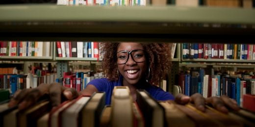 photo of young woman in smiling big in library stacks