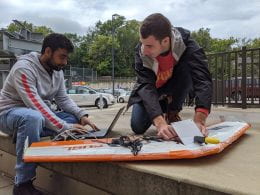 Two male students use a computer and other tools to test a GPS system in a drone.